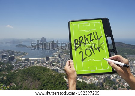 Hands holding Brazil 2014 soccer football tactics board and pen above skyline overlook of Rio de Janeiro