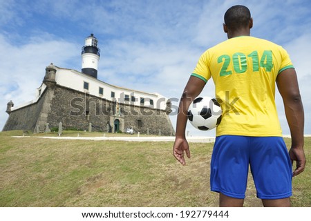 Brazilian football player standing with vintage brown soccer ball at Farol da Barra lighthouse in Salvador