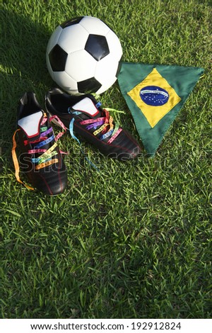 Good luck soccer football boots soccer cleats laced with Brazilian wish ribbons on green grass football pitch with Brazil flag