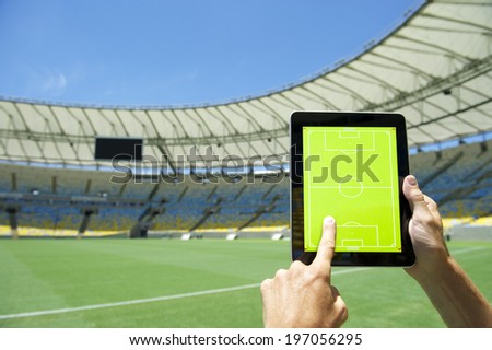 Hands planning match on digital tablet blank tactics board in front of soccer field at football stadium Rio de Janeiro Brazil
