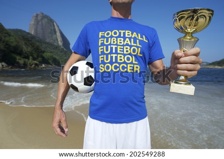 International football player in multi language message t-shirt holding trophy and soccer ball Red Beach Rio de Janeiro Brazil