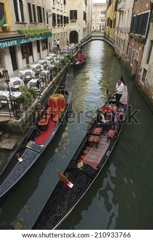 VENICE, ITALY - CIRCA APRIL, 2013: Tourists take ride on colorful gondola outside a restaurant on a small canal.
