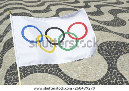 RIO DE JANEIRO, BRAZIL - FEBRUARY 23, 2015: Olympic flag waves in front of the iconic wave pattern of the sidewalk on Copacabana Beach.
