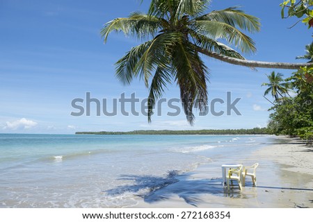 Chair and tables sit in the waves under the shadow of a palm tree on the shore of empty Brazilian beach in Bahia Nordeste Brazil