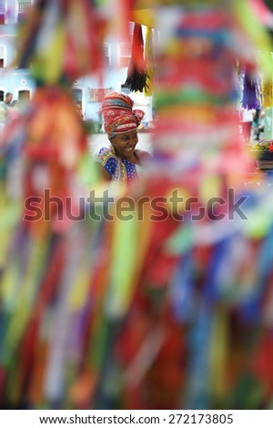 SALVADOR, BRAZIL - MARCH 12, 2015: Baiana vendor selling Brazilian wish ribbons smiles through colorful wall of ribbons in the historic city center of Pelourinho.