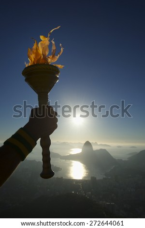 Hand of an athlete holding sport torch against Rio de Janeiro Brazil sunrise skyline with Sugarloaf Mountain