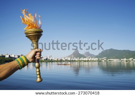 Hand of an athlete wearing Brazil colors sweatband holding sport torch against Rio de Janeiro Brazil skyline with Two Brothers Mountain