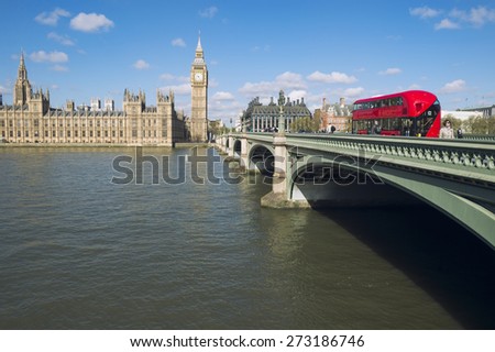 Red double-decker bus passes along Westminster Bridge in front of Big Ben and Houses of Parliament in London England