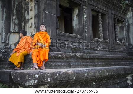 SIEM REAP, CAMBODIA - OCTOBER 30, 2014: Pair of novice Buddhist monks in saffron robes sit on the weathered stone architecture of Angkor Wat temple.