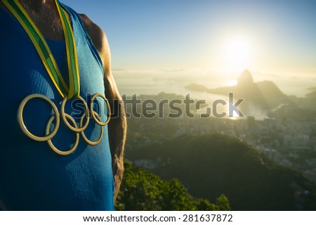RIO DE JANEIRO, BRAZIL - MARCH 05, 2015: Athlete wearing Olympic rings gold medal above city skyline view of Sugarloaf Mountain and Guanabara Bay at sunrise.
