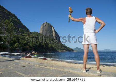 Young athletic man standing with sport torch against Rio de Janeiro Brazil skyline at Red Beach with Sugarloaf Mountain