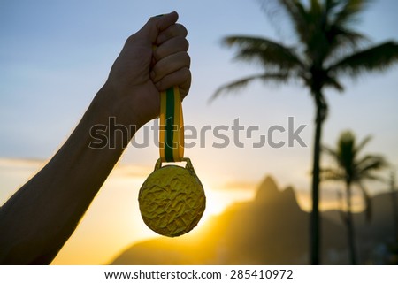 First place athlete holding gold medal in front of the sunset on Ipanema Beach Rio de Janeiro Brazil