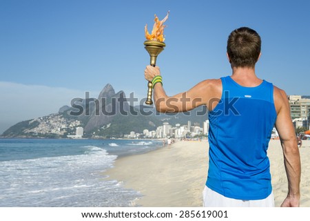 Athlete in athletic uniform standing with sport torch in front of Rio de Janeiro Brazil skyline at Ipanema Beach