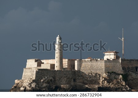 View of el Morro Castle lighthouse architecture in dramatic sunset light against dark cloudy sky
