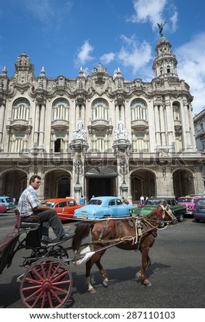 HAVANA, CUBA - JUNE, 2011: Traditional horse and buggy passes row of brightly colored vintage American cars in front of colonial architecture.