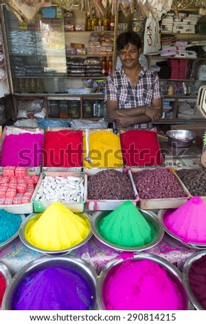MYSORE, INDIA - NOVEMBER 4, 2012: Young Indian vendor stands behind colorful piles of bindi powder in the Devaraja market.