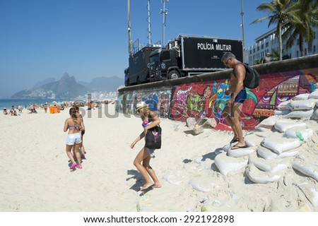 RIO DE JANEIRO, BRAZIL - JANUARY 20, 2015: Beachgoers arrive at Arpoador beach in front of police surveillance trucks set up as a command center in preparation for a busy summer day on Ipanema Beach.
