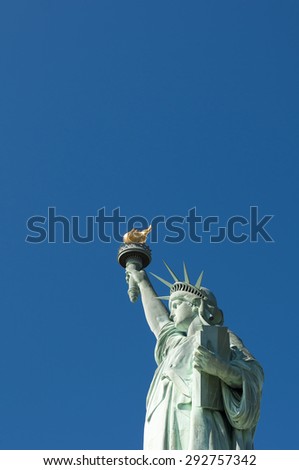 Profile view of the Statue of Liberty holding her torch against clear bright blue sky