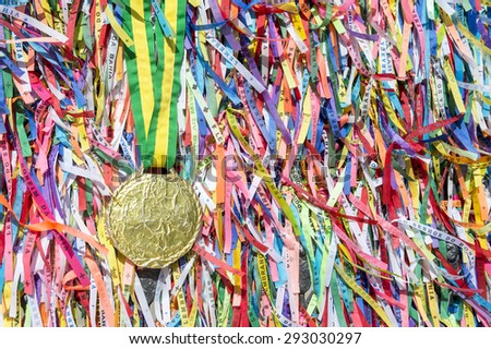 Gold medal hangs from Brazilian colors ribbon in front of a colorful wall of wish ribbons at the Bonfim church