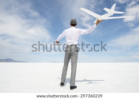 Businessman flying simple inspirational model airplane against blue sky in dramatic white desert landscape