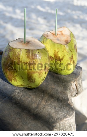 Two green drinking coconuts stand on rustic wood table in dappled sun of Northeast Brazil