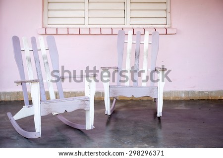 Traditional wooden rocking chairs in front of pink walls on the porch of a rural Cuban house in Vinales, Cuba