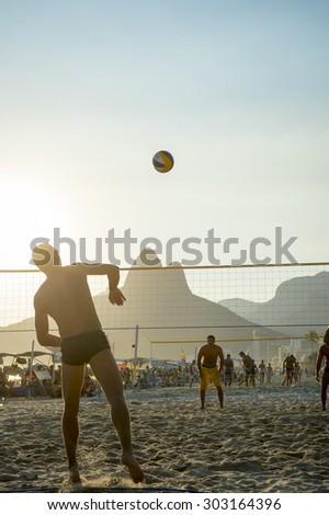 RIO DE JANEIRO, BRAZIL - FEBRUARY 01, 2014: Young Brazilians play a game of beach volleyball against a sunset silhouette of Two Brothers Mountain in Ipanema.