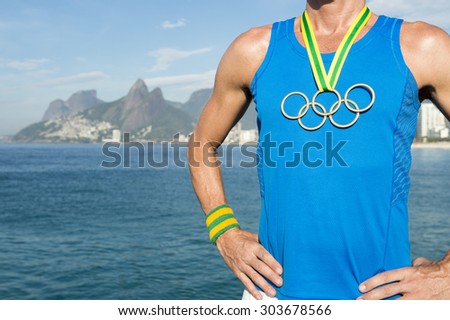 RIO DE JANEIRO, BRAZIL - MARCH 05, 2015: Man stands wearing Olympic rings gold medal in front of city skyline view of Ipanema Beach with Two Brothers Mountain. [illustrative editorial]