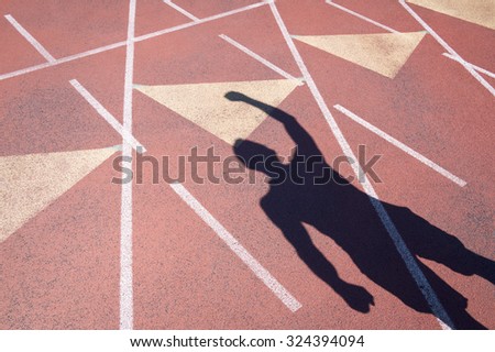 Athlete celebrating with a fist pump casts a shadow on a weathered red running track