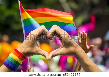 Supporting hands make heart sign and wave in front of a rainbow flag flying on the sidelines of a summer gay pride parade Сток-фото © 