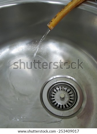 Water flowing from the plastic hose in a sink metal close-up