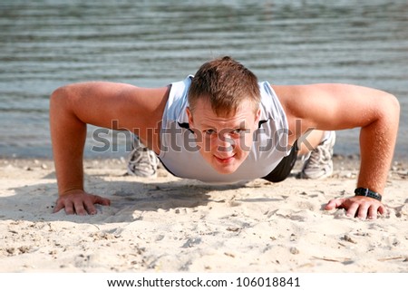 Young caucasian male in sportswear doing push ups at the beach
