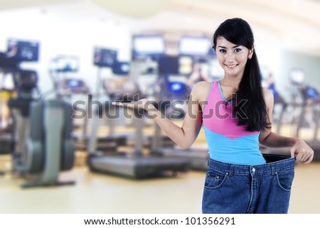 Weight loss concept: Beautiful Asian woman showing her old jeans, shot in fitness center