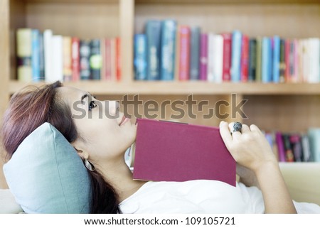 Portrait of smiling woman holding book and lying on couch