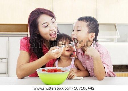 Mother and children eating healthy snack - fruit salad. Shot in the kitchen