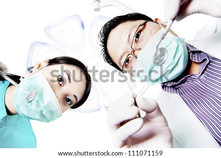 photo of an asian dentist with his assistant, as seen from the patient's point of view, lying in the chair