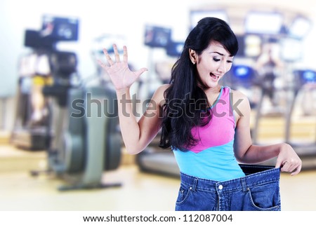Happy asian woman posing in gym with her old big pants