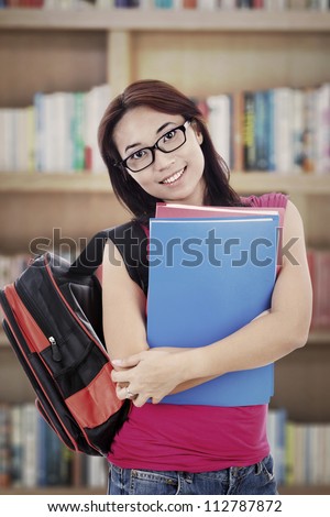 Portrait of smiling female college student carrying folders. shot in library