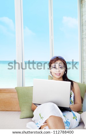 Portrait of beautiful asian woman working on laptop with ocean view on the window
