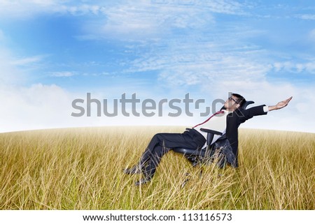 Businessman on his office chair with his arms and feet up in the air. Shot outdoor in marshes