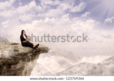 Young businesswoman is relaxing while working with her laptop on a mountain