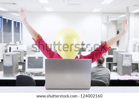 Businesswoman with face covered with balloon expressing happiness. Shot at office