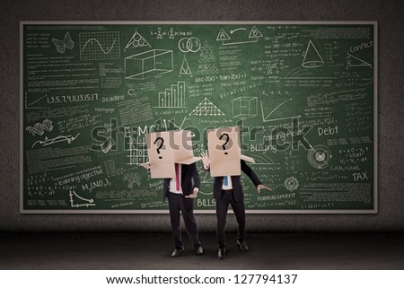 Two businessmen with question mark boxes standing in front of blackboard
