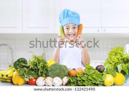 Chef boy is holding carrot and cucumber at home
