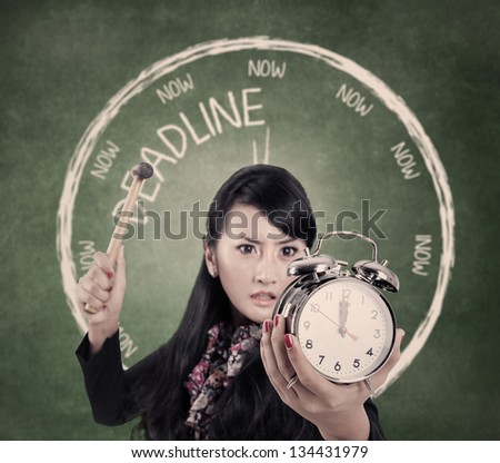 Angry business woman smashing an alarm clock by using hammer