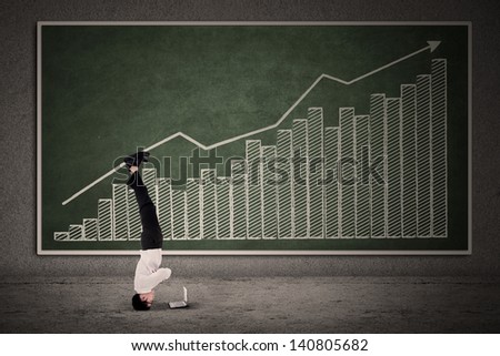 Businessman acrobatic move on profit bar chart while looking at a laptop