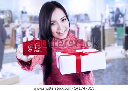 Asian female shopper showing gift card and box at the mall