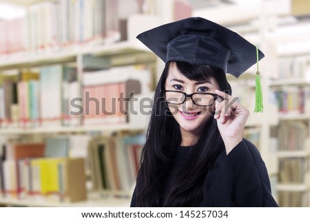 Asian graduate in graduation gown with glasses pose at library