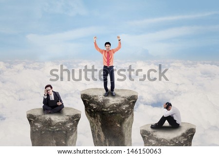 Business people on top of rocks with one winner exulting above clouds