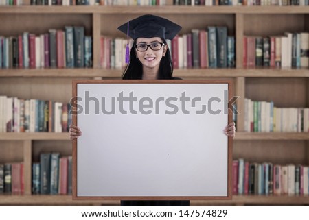 Happy graduation student girl with blank whiteboard in library